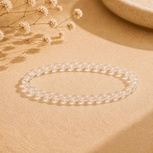 Natural clear quartz bracelet with polished transparent round beads displayed on neutral fabric in warm light