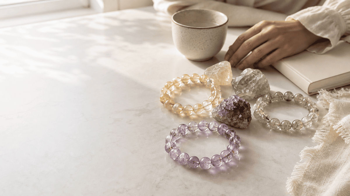 Crystal bracelets with healing stones arranged beside a cup and notebook, featuring amethyst, citrine, and clear crystal beads
