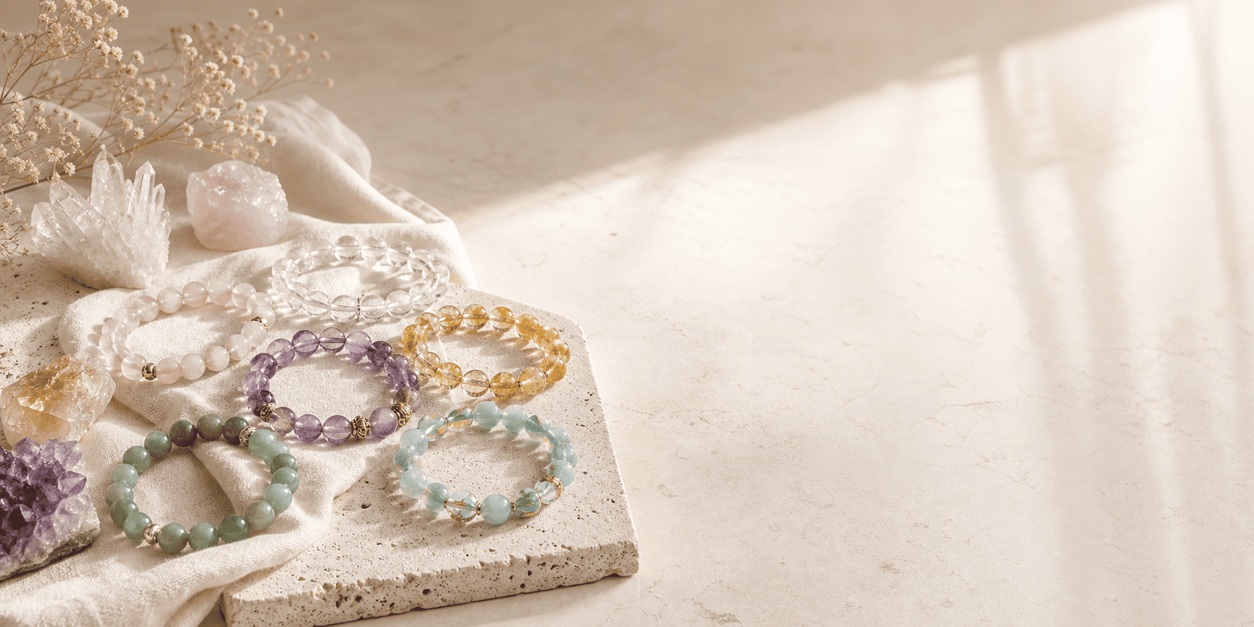 Natural crystal bracelets arranged on ivory linen with rose quartz, clear quartz, citrine, amethyst, and green gemstones for a premium jewelry hero image.