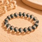 Green phantom quartz bracelet with round beads and clustered green inclusions on a sunlit textured surface