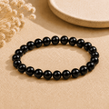 Real black obsidian bracelet with polished round beads displayed on neutral fabric