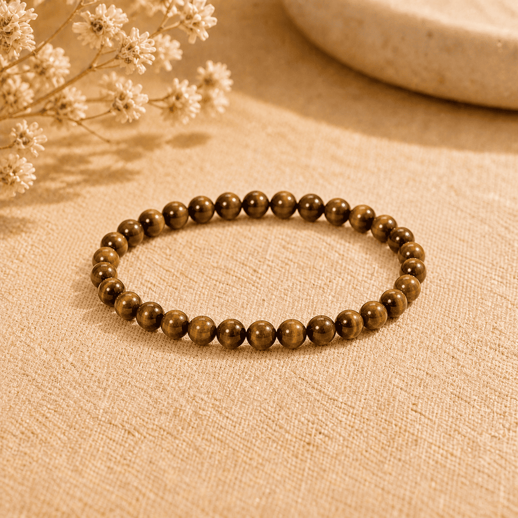 Tiger eye stone bracelet with small polished round beads displayed on neutral fabric in warm light