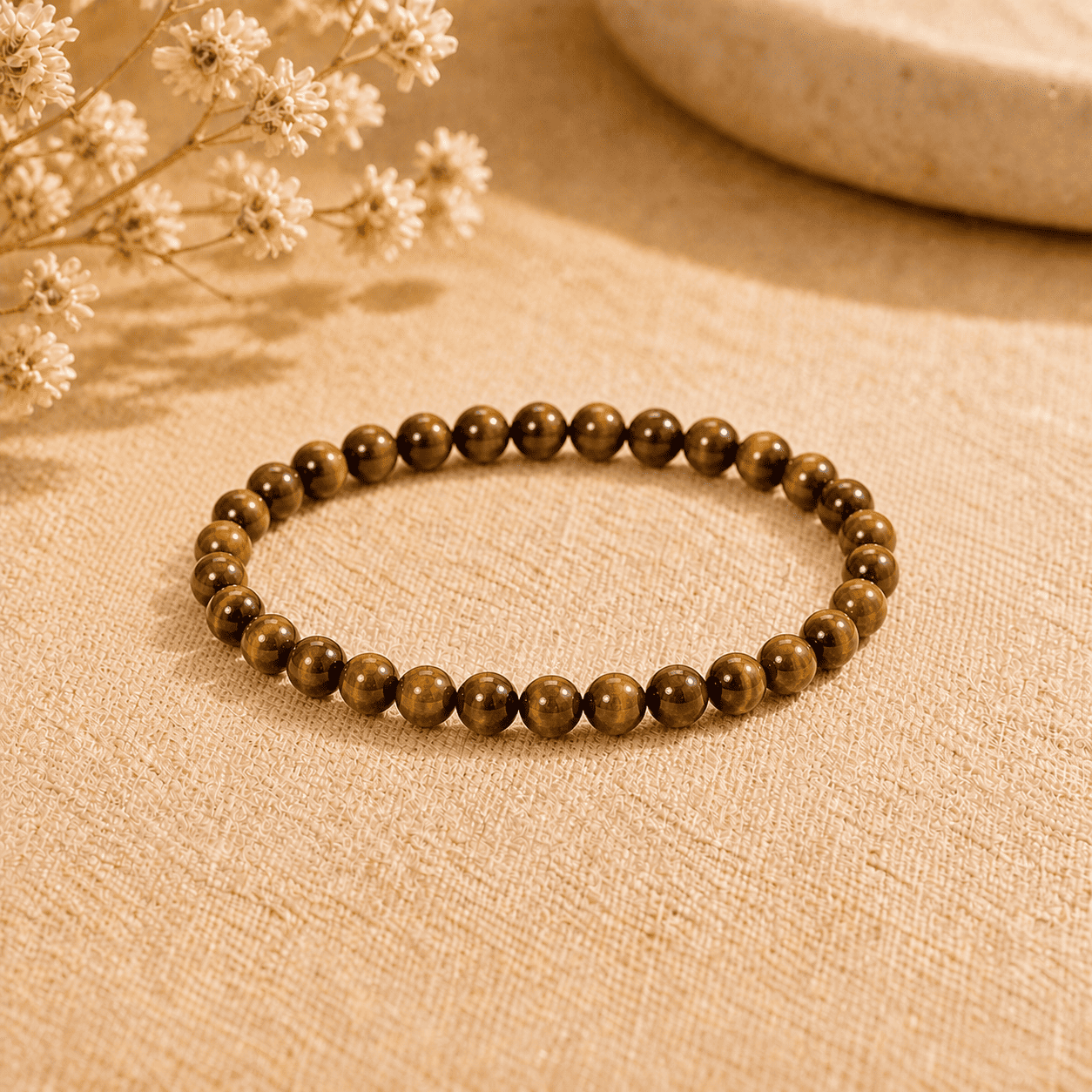 Tiger eye stone bracelet with small polished round beads displayed on neutral fabric in warm light